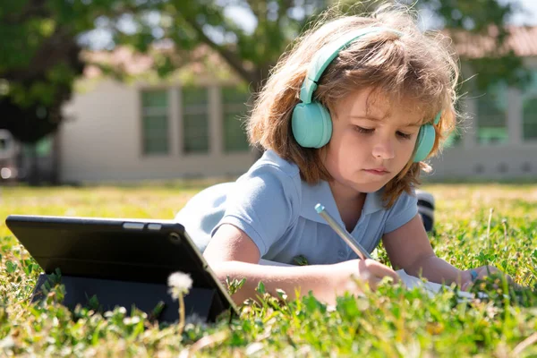 Des devoirs d'enfant à l'extérieur dans une cour de récréation. Petite écolière avec tablette dans le parc sur herbe. Auto-éducation, apprentissage des enfants et études sur le parc de l'école. Développement précoce pour les enfants. — Photo