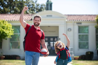 Baba oğluna okula kadar eşlik ediyor. Sırt çantalı ilkokul öğrencisinin ebeveyni ve öğrencisi..