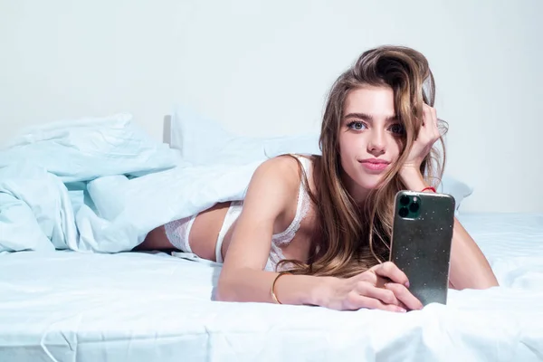 속옷 차림의 아름다운 관능적 인 여성 이 전화기를 들고 침대에 누워 있는 모습. — 스톡 사진
