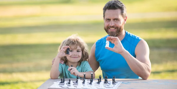 Son laying on grass and playing chess with father. Child play chess. — Stock Photo, Image