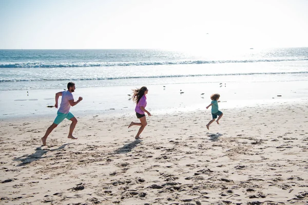 Feliz joven familia correr y saltar en la playa de verano. Concepto de familia amigable y de vacaciones de verano. Niño con padres corriendo y saltando. —  Fotos de Stock