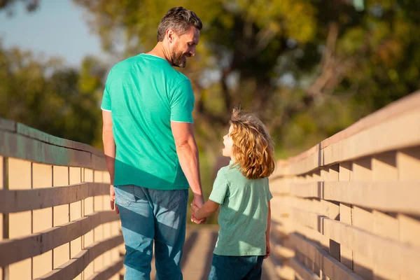 Achteraanzicht van vader en zoon wandelen op bosrijke brug buiten. Vader en zoon praten, hebben plezier in de natuur. Ouderschap, ouderschap, kinder- en gezinsleven. — Stockfoto