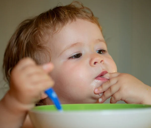 Lame sabrosos dedos. Retrato de niño caucásico lindo con cuchara. Bebé desordenado hambriento con plato después de comer puré. — Foto de Stock