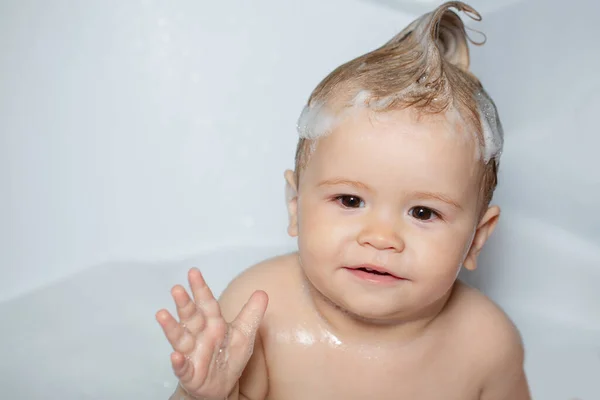 Todler arccal zuhanyozik. Egy kisfiú a fürdőkádban bolyhos szappanbuborékkal. Vicces boldog baba fürdik fürdőkádban vízzel és habbal. Gyerek higiénia. — Stock Fotó