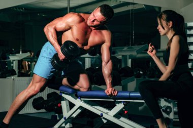 Antrenör dambıl egzersizi. BoodyBuilder çifti. Spor salonunda ağır halterlerle çalışan bir kadına yardım eden yakın bir arkadaş. Sporcu konsepti. Spor kadını..