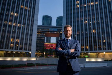 Ofis yakınında takım elbiseli mutlu bir işadamı, başarılı bir işveren geceleri gökdelen bürosunun yanında dururken anlaşma yapıyor..