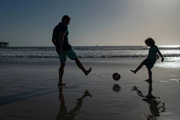 夏の日に子供の男の子とパパ。夏の日に遊んでいる子供の男の子とお父さん。父と息子はビーチでサッカーやサッカーをします。スポーティファミリーのコンセプト. — ストック写真