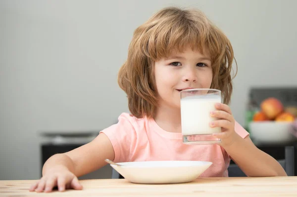 Lindo niño pequeño con vaso de leche en la mesa en la cocina. Niño desayunando. Niño comiendo alimentos saludables. Leche ecológica con calcio. Pequeño niño disfruta de delicioso yogur nutritivo sin lactosa. — Foto de Stock