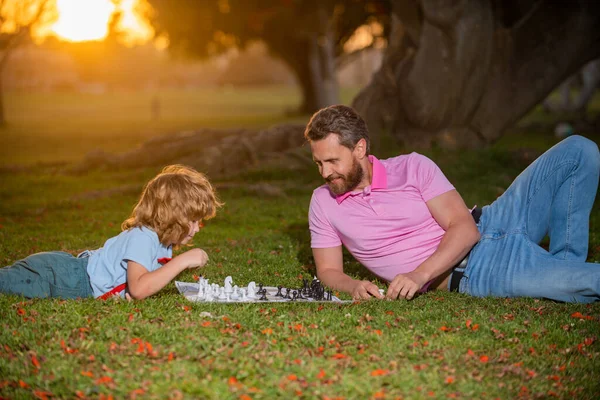 Joyeux famille en plein air. Père et fils jouent aux échecs dans Spring Garden. Jeune garçon battant un homme aux échecs. — Photo