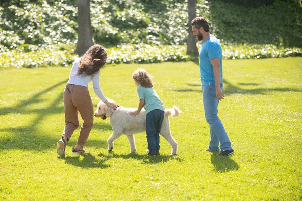 Mutter, Vater und Sohn laufen mit Hund im Park. Glückliche junge Familie, die zusammen Zeit draußen in der grünen Natur verbringt. Niedliches Familienporträt. — Stockfoto