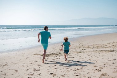 Baba ve oğul denizde koşuyor. Baba ve çocuk dışarıda eğleniyor. Aile seyahati, tatil, babalar günü konsepti.