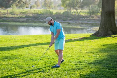 Golf sopası, sıcak bir akşamda bir golf sahasındaki çimlerin üzerinde duran bir adam..