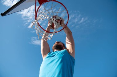 Basketbolcu mavi gökyüzü arkaplanına karşı şut atıyor.