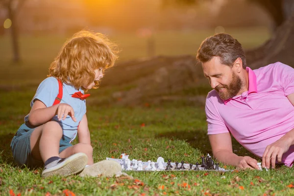 Otec a syn hrají šachy a tráví spolu čas v parku. Aktivní lidé baví a hrát šachy v parku, trávit čas s dítětem. — Stock fotografie