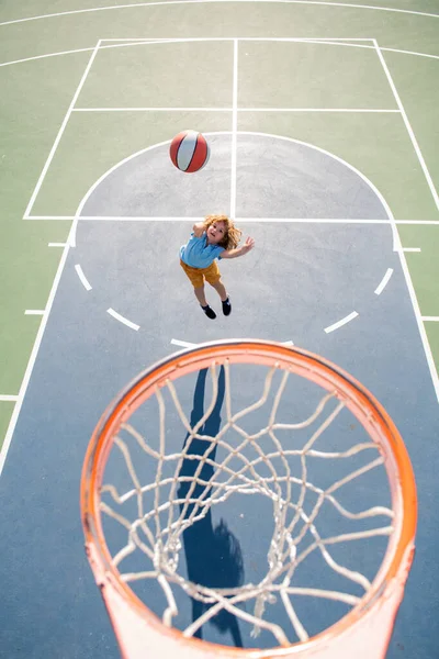 Criança em salto uniforme de basquete com bola de cesta para tiro na quadra de basquete. — Fotografia de Stock