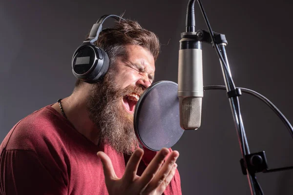 Sänger in einem Tonstudio. Ausdrucksstarker bärtiger Mann mit Mikrofon. Soundproduzent. Karaoke-Unterzeichner, Sänger. — Stockfoto