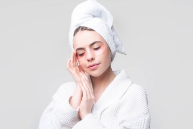 Göz bandı takan bir kadın. Sakin, rahat bir kadın taze, sağlıklı bir cilde sahip, gözleri kapalı, gözlerinin altına kolajen bantlar takıyor, kafasına havlu takıyor, yüz bakımı yaptırıyor..