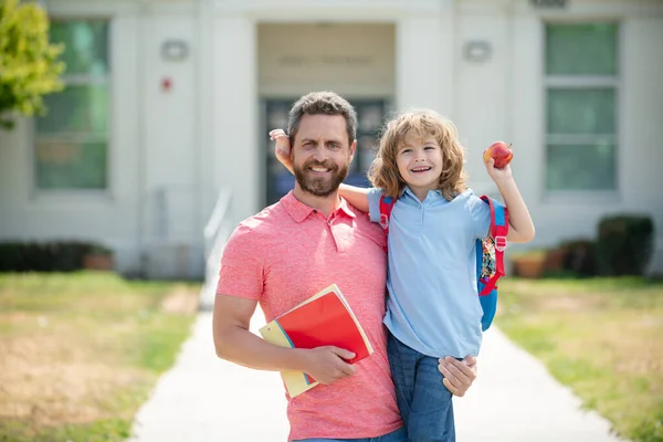 Portrait de professeur et élève heureux. Parent et élève de l'école primaire vont de pair. Professeur en t-shirt et écolier mignon avec sac à dos près du parc scolaire. — Photo