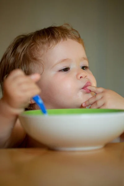 Petit bébé drôle dans la cuisine manger avec les doigts de la plaque. Lécher les doigts savoureux. — Photo