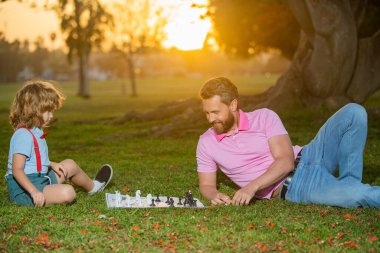 Baba oğluyla satranç oynar. Aile oyunu dışında. Küçük çocuk ailesiyle satranç oynuyor. Bilişsel gelişim. Entelektüel çocuklar oyunu. Akıllı çocuklar..