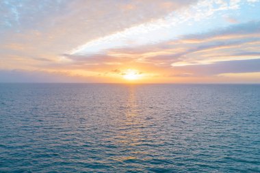 Gün batımında gökyüzü ve bulutların arasında güneş olan sakin bir deniz. Okyanus ve gökyüzü arkaplanı, deniz manzarası.