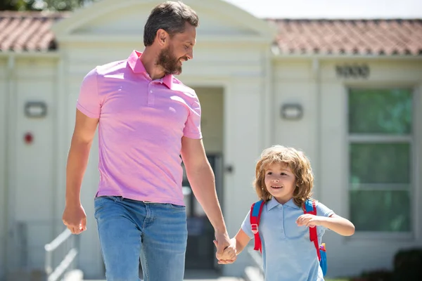 Father and son run with father after come back from school. School, family, education and outdoor concept. First day at school. Parent leads a little child school boy in first grade.