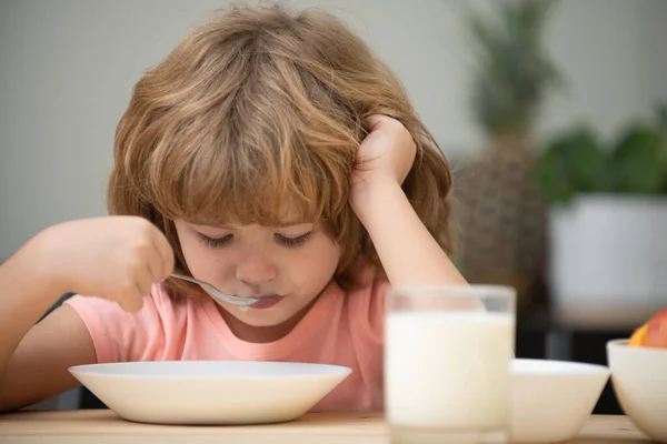 Child eating healthy food at home. Unhappy child have no appetite. Upset little kid refuse to eat organic cereals with milk. Baby eat soup with spoon.