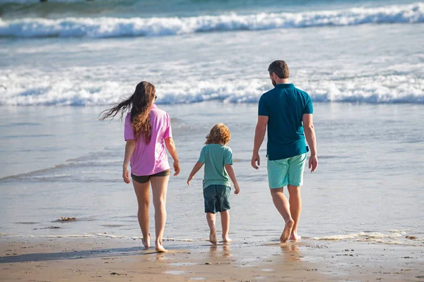 Achteraanzicht van familie op het strand. Mensen hebben plezier op zomervakantie. Vader, moeder en kind houden elkaars hand vast tegen de blauwe zee. Vakantie reisconcept. Zomervakantie familie. — Stockfoto