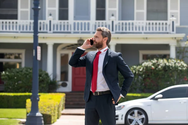 Business man holding mobile cell phone using app texting sms message wearing suit. Young urban professional man using smartphone at home. Real estate agent.