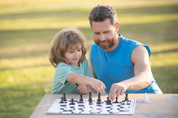 Father and son playing chess spending time together outdoor. Kid play chess.