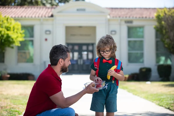 School jongen gaat naar school met vader. Kleine schooljongen die buiten lekker luncht. Lunch op school voor kind. — Stockfoto