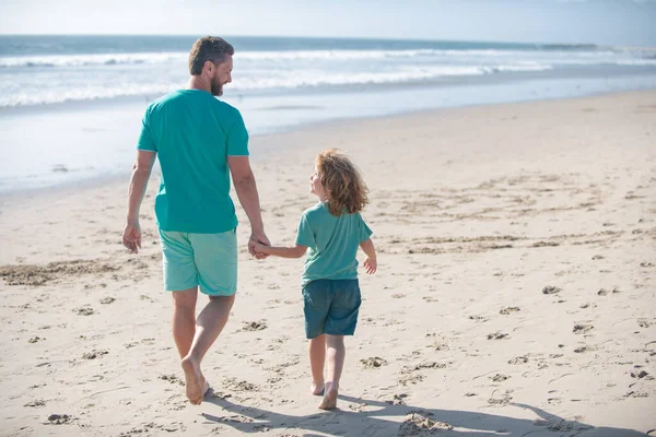 Pai e menino de mãos dadas e caminham juntos. Pai e filho caminhando na praia de verão. Conceito de família amigável e de férias de verão. — Fotografia de Stock
