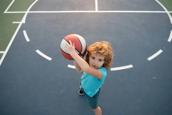 Roztomilý chlapeček držící basketbalový míček se snaží skórovat. Sport pro děti, pohled shora. — Stock fotografie