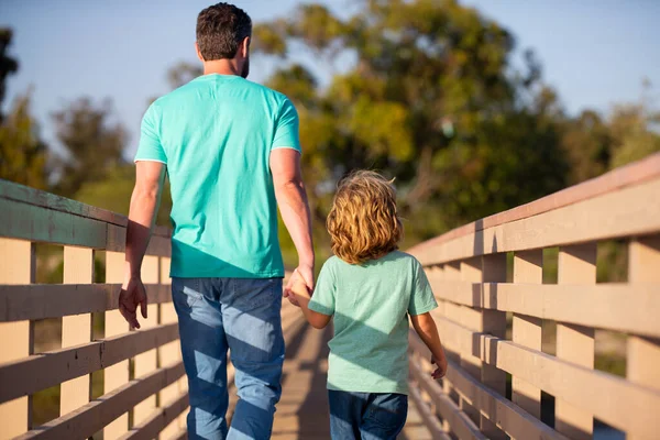 Achteraanzicht van vader met zoon lopend op houten brug buiten. — Stockfoto