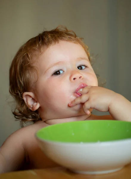 Portrait of cute Caucasian child kid with spoon. Hungry messy baby with plate after eating puree. — Stock Photo, Image