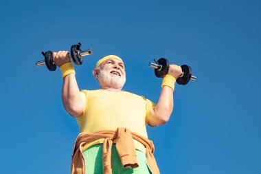 Kıdemli adam dambılı kaldırıyor. Yetmişli yaşlardaki kıdemli adam antrenman yapıyor ve ağırlık kaldırıyor. Kıdemli sporcu dambılları kaldırıyor. Yaşlı adam egzersizi..