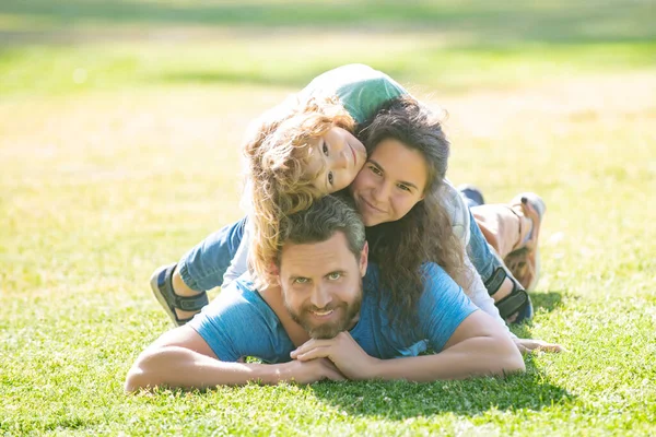 Familie umarmt und umarmt, auf Gras im Park liegend. Porträt einer glücklich lächelnden Familie beim Entspannen im Park. — Stockfoto