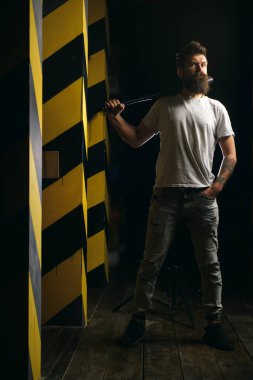 Şehir merkezinde beyzbol sopası tutan güçlü sakallı, tehlikeli görünümlü bir adam. Tehlike ve saldırganlık kavramı. Dikkat et, dikkatli ol. Sokak serserisi ve suç kavramı.