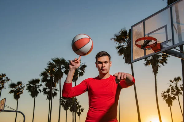 Basketballspieler schießt Ball in Reifen Outdoor Court. Stadtjugendspiel. Handspinnender Korbball. Basketball auf dem Finger balancieren. — Stockfoto