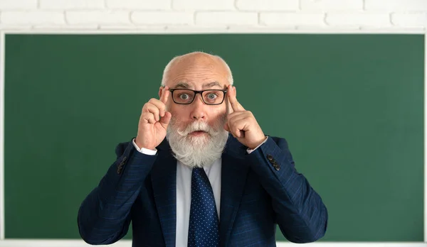 Funny senior professor in glasses. Surprised grey hair professor near blackboard. Think.