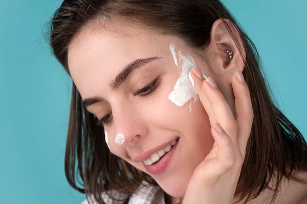 Mooi meisje model met natuurlijke make-up aanbrengen moisturizer crème op mooi gezicht. — Stockfoto