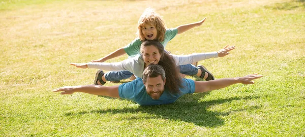 Family leisure time. Family lying on grass in park. Parents giving child piggybacks in park. — Stock Photo, Image