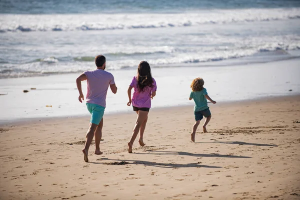 幸せな若い家族が走り、夏のビーチでジャンプします。親と一緒に子供が走ってジャンプします。フレンドリーな家族と夏休みの概念. — ストック写真