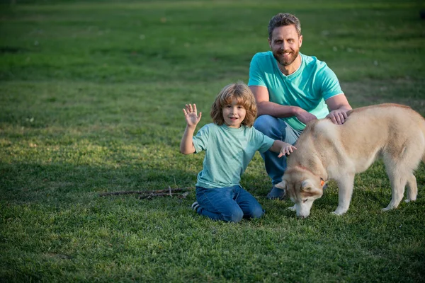 Hijo y padre como familia con perro jugando juntos en el parque de verano en la hierba. Niño con su amigo mascota. —  Fotos de Stock