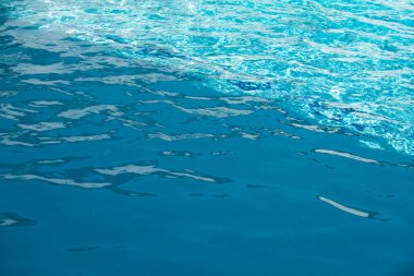 Mavi havuz suyu arka planı. Bulanık şeffaf, durgun su yüzeyi dokusu. Güneş ışığı altında su dalgaları kopyalama alanı ile.