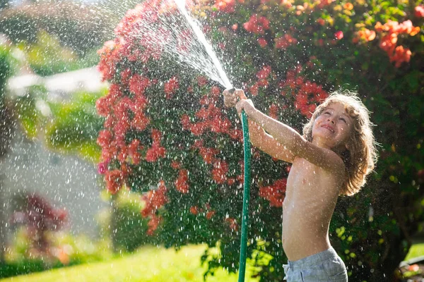 Glücklicher kleiner Junge, der Spaß im heimischen Garten hat. Kind hält Gartenschlauch in der Hand. Aktive Outdoor-Spiele für Kinder im Hinterhof zur Erntezeit — Stockfoto