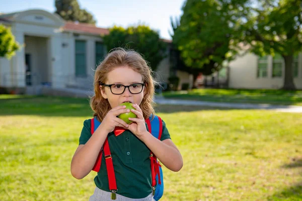 Παιδί με σακίδια στο σχολικό πάρκο. Μαθητές με σακίδια στην ύπαιθρο. Μαθητευόμενος τρώει μήλο. — Φωτογραφία Αρχείου