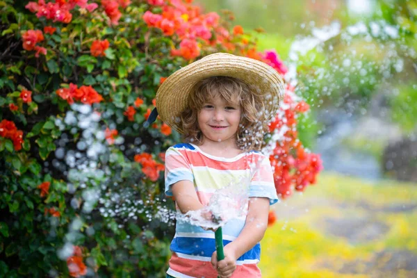 Симпатичный маленький мальчик в соломенной шляпе смеется, распыляя воду из шланга.. — стоковое фото