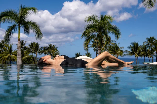 Lüks bir tatil köyünde sonsuz yüzme havuzunda güneşlenen bir kadın.. — Stok fotoğraf