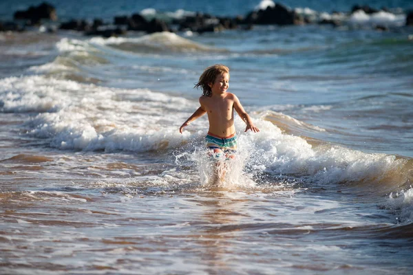 Dziecko przepływające przez wodę blisko brzegu wzdłuż plaży morskiej. Chłopiec biegnie wzdłuż wybrzeża. Reszta dzieci na wakacjach letnich. — Zdjęcie stockowe